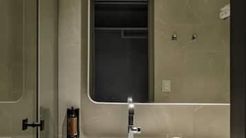 Un baño moderno con cabina de ducha de vidrio, un lavamanos blanco con espejo y una pequeña botella de jabón en la encimera.