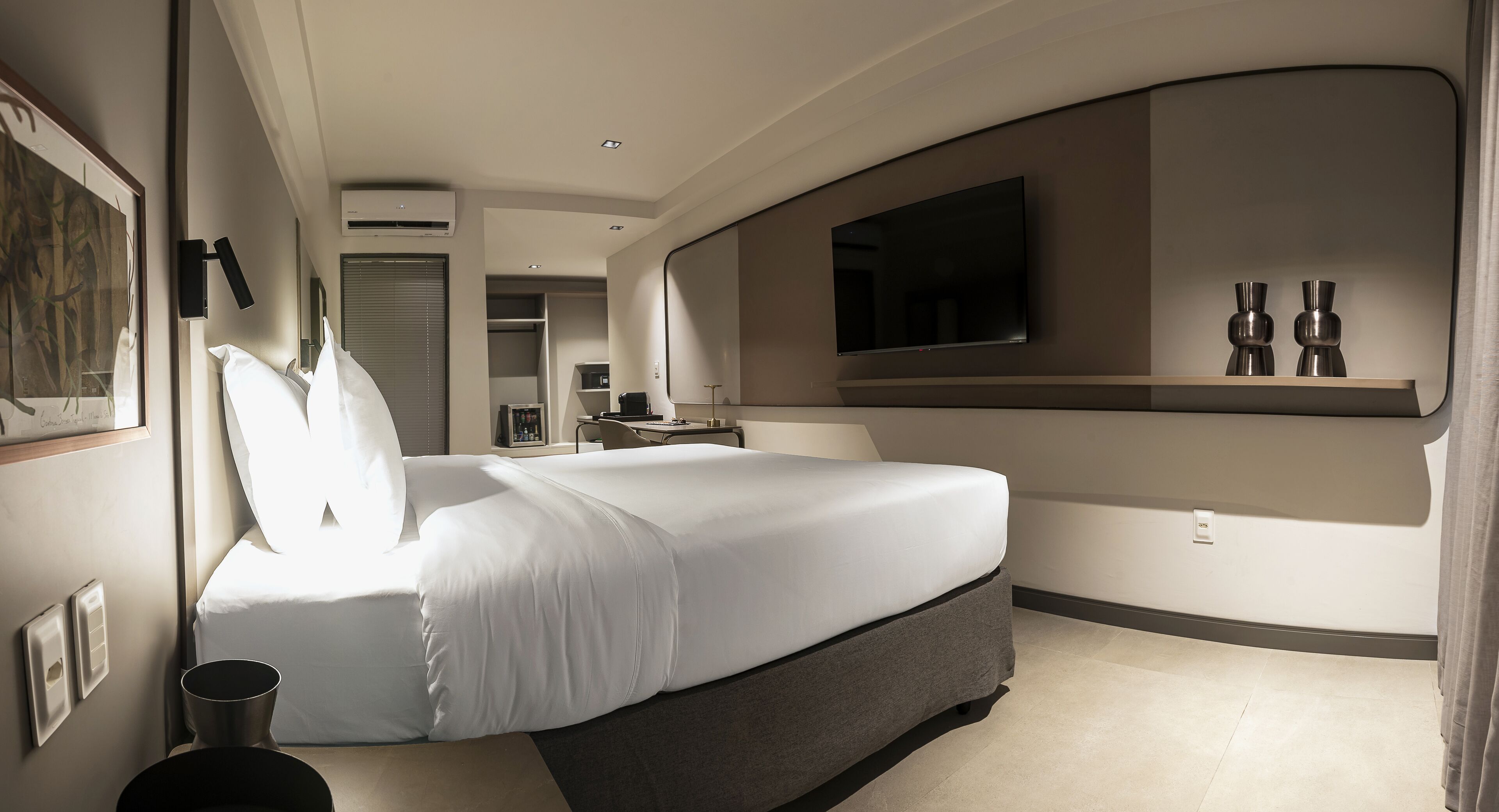 Una habitación de hotel moderna con una cama grande, un televisor de pantalla plana en la pared y una mesita con un florero.