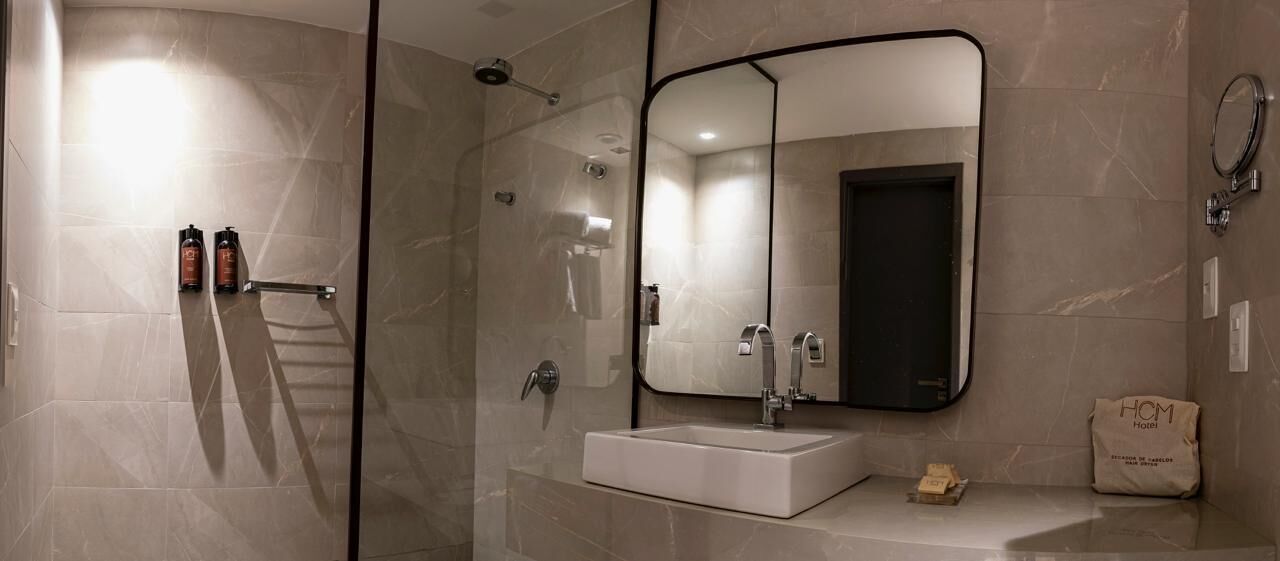 Un baño moderno con cabina de ducha de vidrio, un lavamanos blanco, un espejo grande y un perchero para toallas.