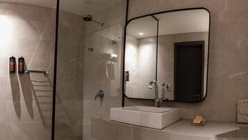 Un baño moderno con cabina de ducha de vidrio, un lavamanos blanco, un espejo grande y un perchero para toallas.