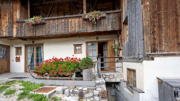 A traditional wooden building with a stone entrance, a flower bed with red flowers, and a balcony with hanging flower baskets. - Casa Lacedel 1 on Ski slopes (Cortina d´Ampezzo)