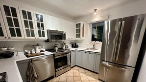 A modern kitchen with white cabinets, stainless steel appliances, and a tiled floor.
