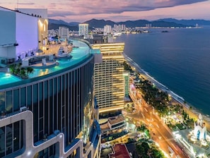 A high-rise hotel with a rooftop infinity pool, a modern glass facade, and a view of the coastline. - Panorama Apartment Sunset Nha Trang City (Nha Trang)