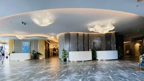 Un hall d’entrée spacieux, doté d’un sol en marbre, d’un comptoir de réception et d’un éclairage moderne au plafond.