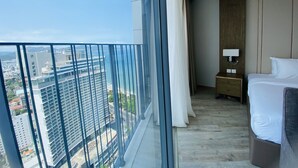 Une chambre d’hôtel avec une grande fenêtre, un lit, une table de chevet et une vue sur la ville et l’océan.