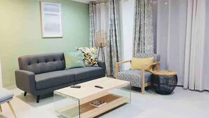 A modern living room with a grey sofa, a small round coffee table, and a patterned armchair. - Contemporary 2 bed in Suburbs - 2080 (Bulawayo)