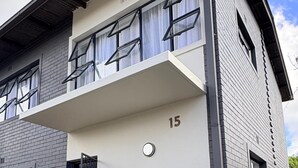A modern two-story building with a flat roof, a balcony, and a potted plant in the entrance. - Chic Modern House on Neasden - 2085 (Bulawayo)