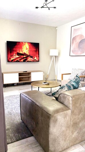A living room with a flat-screen TV mounted on the wall, a sofa, a coffee table, and a floor lamp. - Chic Modern House on Neasden - 2085 (Bulawayo)