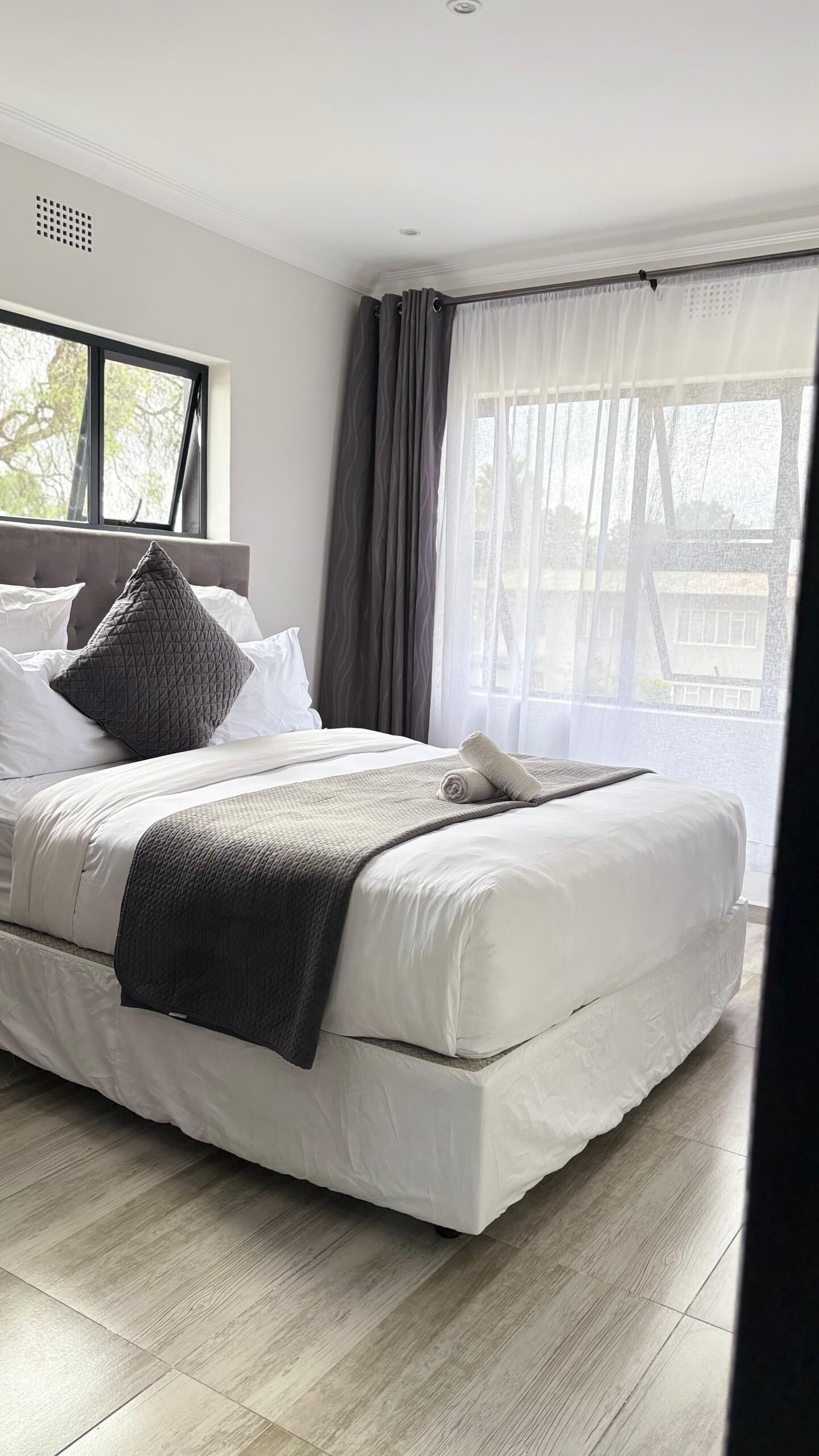 Une chambre à coucher moderne avec un grand lit, une fenêtre avec des rideaux et une vue sur l’extérieur.