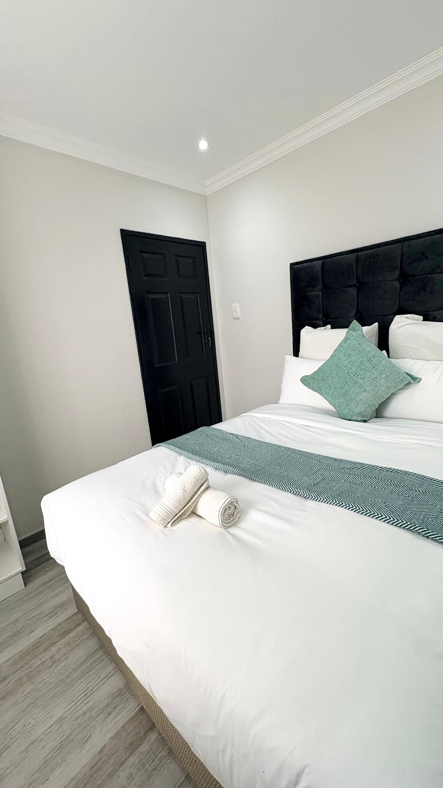 Une chambre d’hôtel avec un grand lit, une tête de lit sombre, une porte et un plancher de couleur claire.