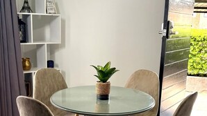 A round glass table with four chairs, a potted plant, and a white shelving unit with decorative items. - Chic Modern House on Neasden - 2085 (Bulawayo)