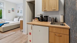 A compact hotel room with a kitchenette, a bed, a small bathroom, and a view of greenery outside. - Vorstadtoase für 2 - 2023 eröffnet - Netflix, Parken, Queensize-Bett, Nähe BER (Eichwalde)