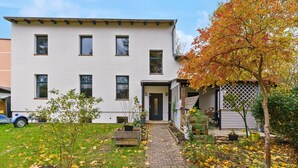 A two-story white building with a front door, windows, and a paved pathway leading to the entrance. - Vorstadtoase für 2 - 2023 eröffnet - Netflix, Parken, Queensize-Bett, Nähe BER (Eichwalde)