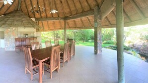 Un espace de restauration en plein air doté d’un toit de chaume, de piliers en pierre et offrant une vue sur un jardin.