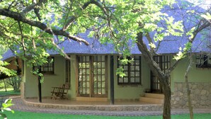 A house with a thatched roof, a porch with a bench, and a stone wall.