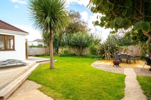 A backyard with a wooden deck, a palm tree, a barbecue area, and a dining table.