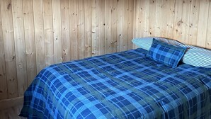 Une pièce aux murs en bois et un lit recouvert d’une couette à carreaux bleus.
