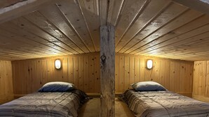 Une pièce avec deux lits, des murs en bois et un pilier central en bois.