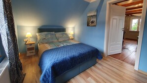 Une chambre à coucher comprenant un lit, deux tables de chevet, une commode, une fenêtre et une porte donnant sur une autre pièce.
