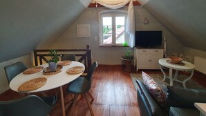 Une pièce mansardée chaleureuse, aménagée avec une table à manger, des chaises, un téléviseur et une fenêtre avec des rideaux.