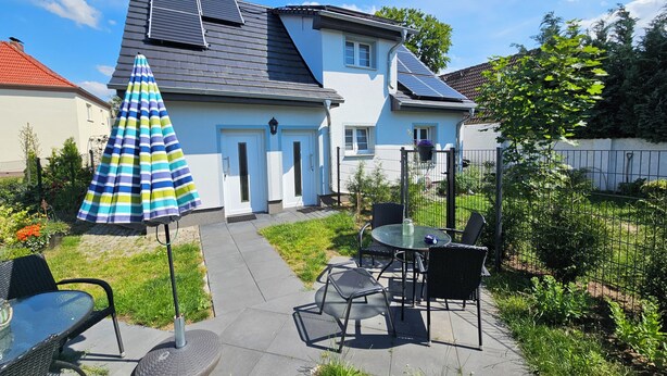 Une maison dotée de panneaux solaires, une terrasse avec des meubles d’extérieur et un jardin.