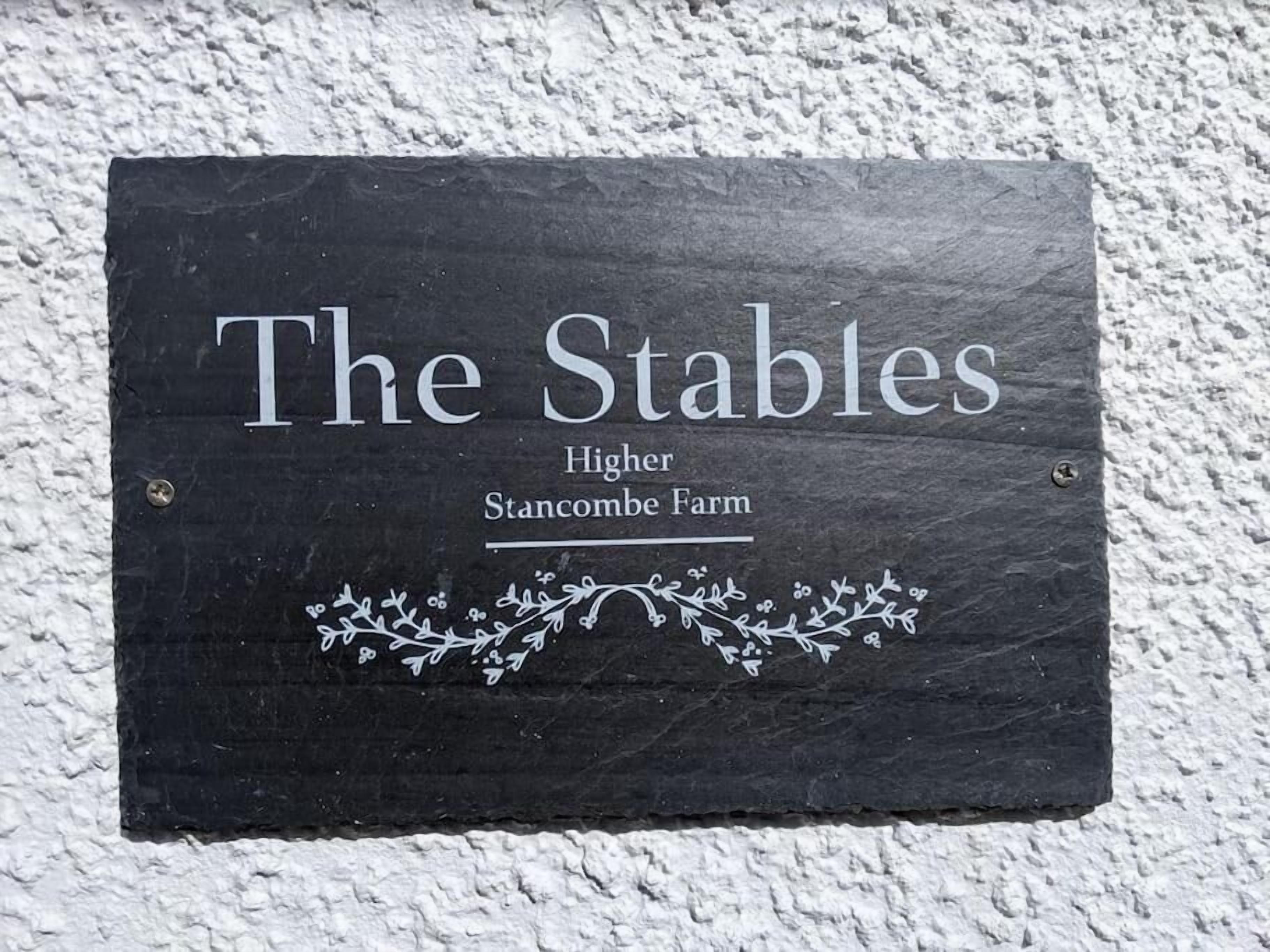 A black slate sign with white lettering that reads 'The Stables Higher Stancombe Farm.'