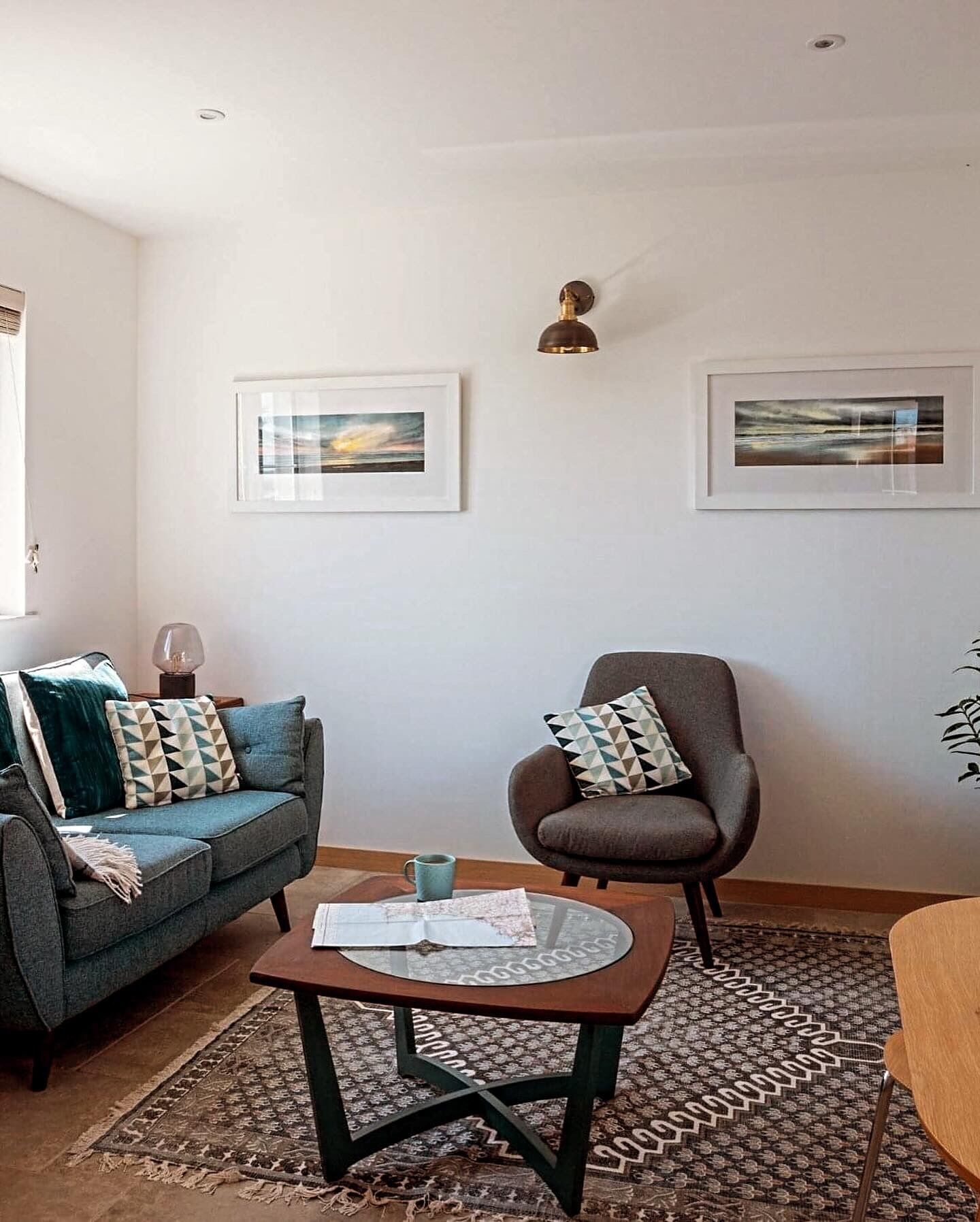 Ein Wohnzimmer mit Sofa, Sessel und Couchtisch, mit Kunstwerken an den Wänden und einem gemusterten Teppich.