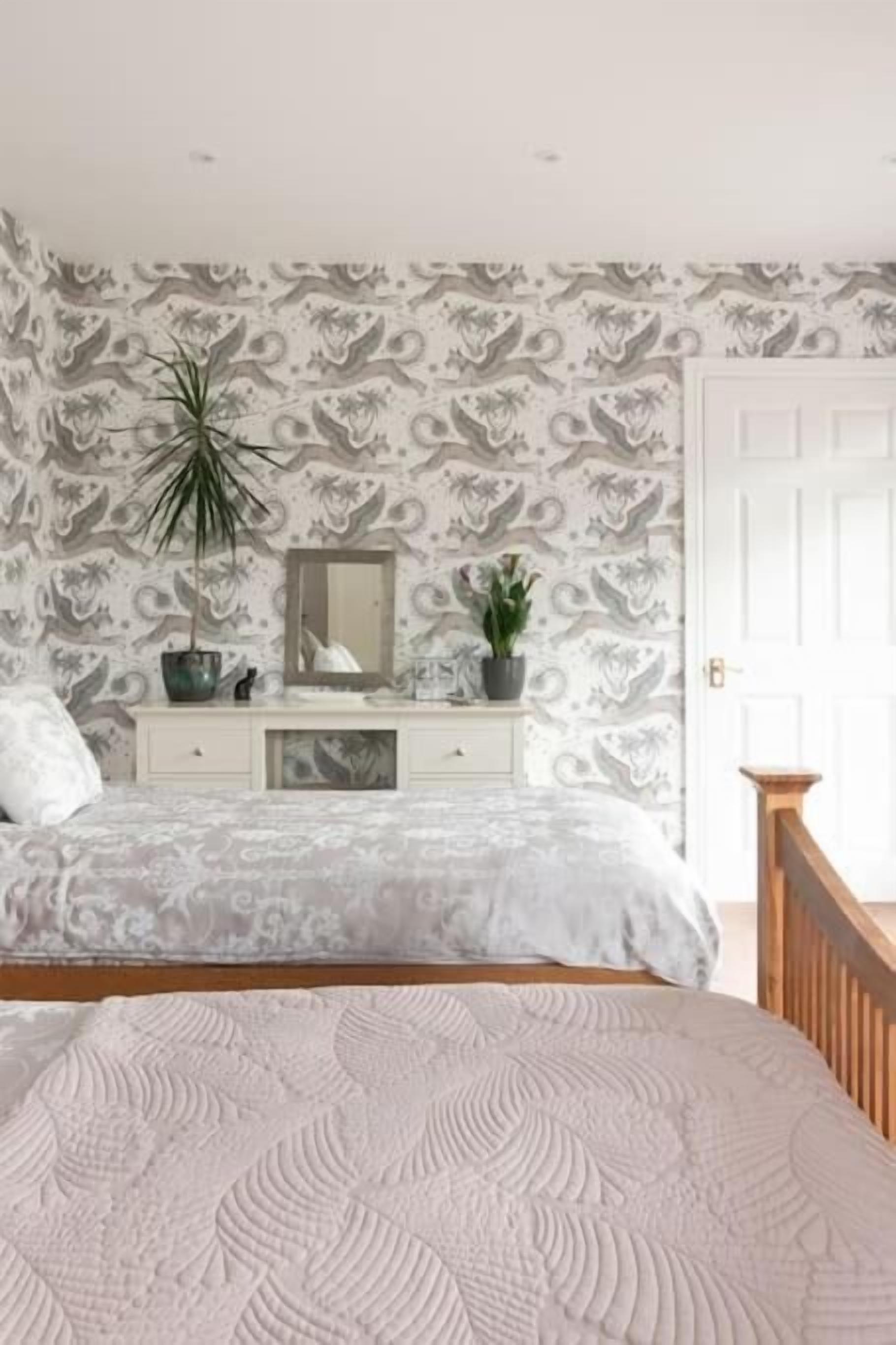 A bedroom with a bed, a dresser, a mirror, and two potted plants.