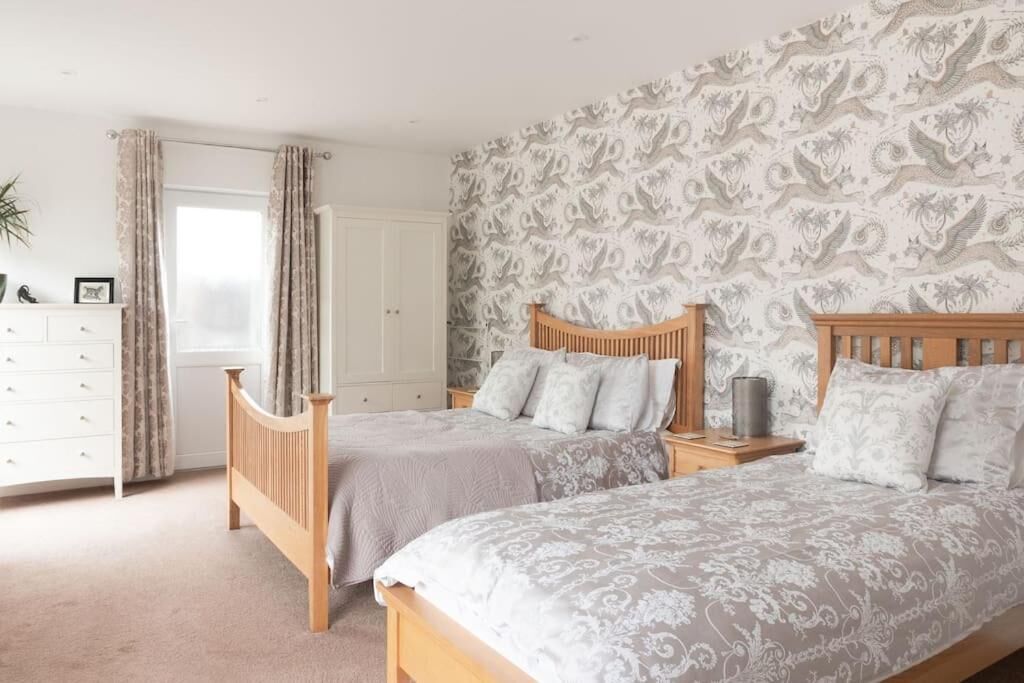 A bedroom with two wooden beds, a white dresser, and a patterned wallpaper.
