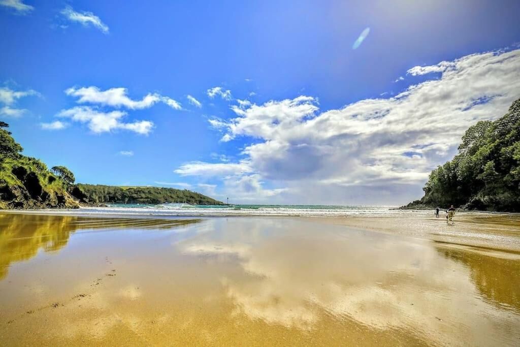 Une plage aux eaux calmes, sous un ciel dégagé, bordée de falaises rocheuses.