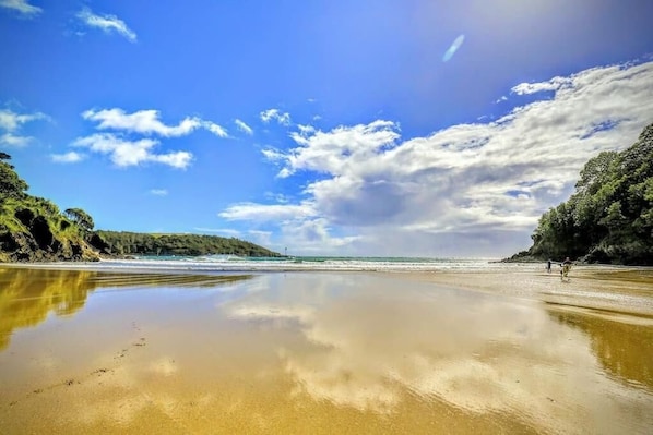 A beach with calm waters, clear skies, and rocky cliffs.