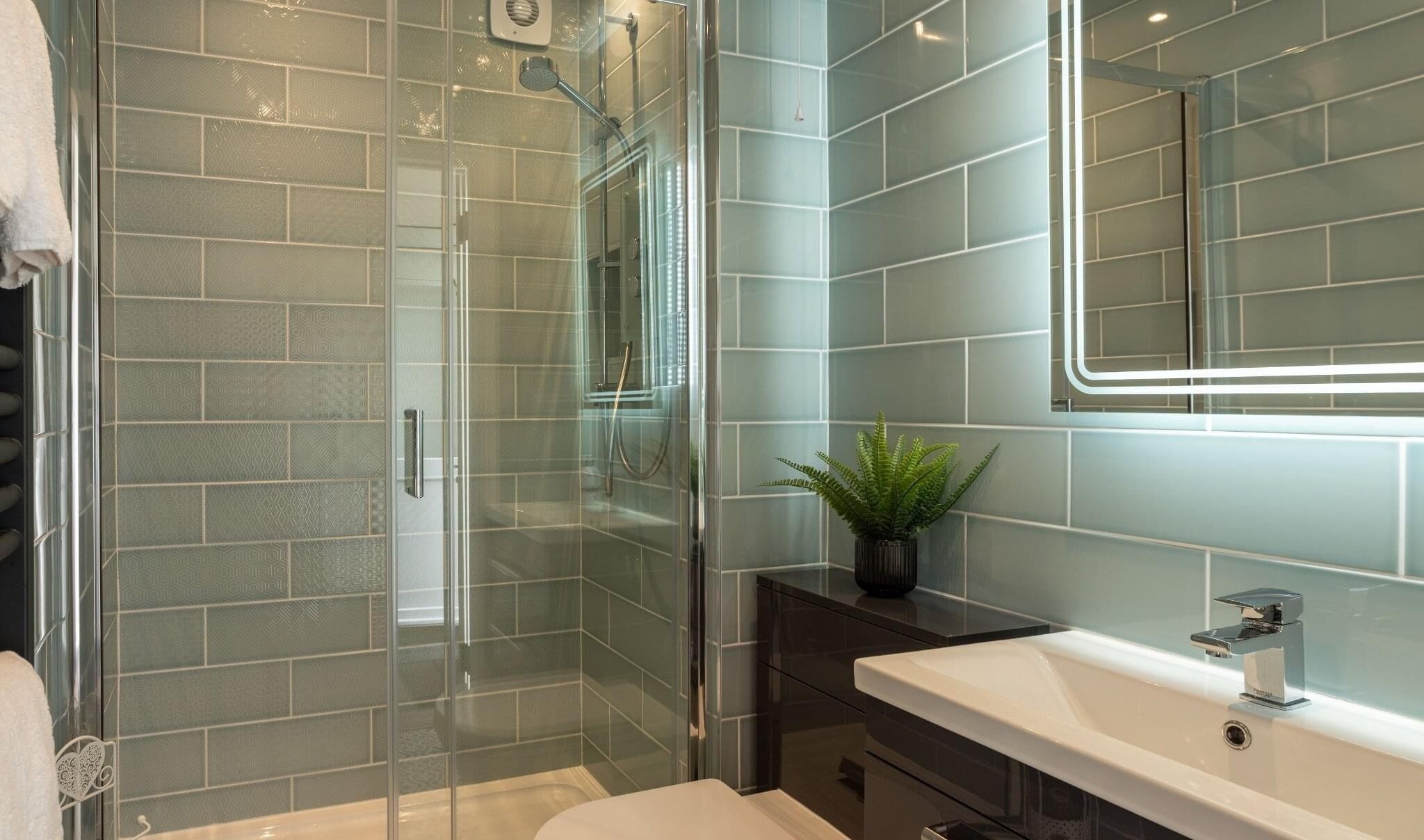 A modern bathroom with a glass-enclosed shower, a white sink, and a mirror with LED lighting.