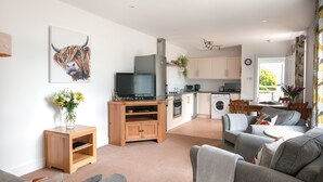 A modern living room with a flat-screen TV, a wooden side table with a vase, and a grey sofa. - Higher Stancombe Holiday Cottages (Kingsbridge)