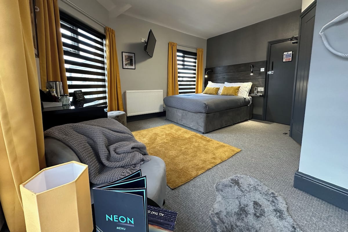 A hotel room with a bed, a sofa, a desk, and a window with blinds.
