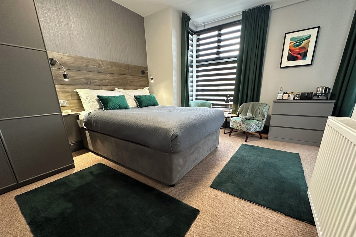 A hotel room with a bed, a chair, a desk, and a radiator.