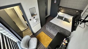 A compact hotel room with a bed, a small seating area, a radiator, a mirror, and a minibar. - Hotel Neon (Blackpool)