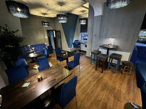 Interior de restaurante com piso de madeira, assentos estofados em azul e iluminação pendente.