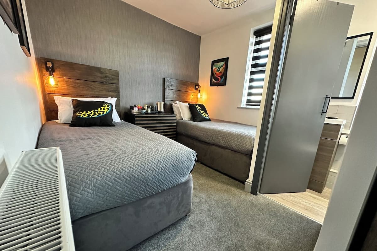 A modern bedroom with two beds, a dresser, a nightstand, and a window with blinds.