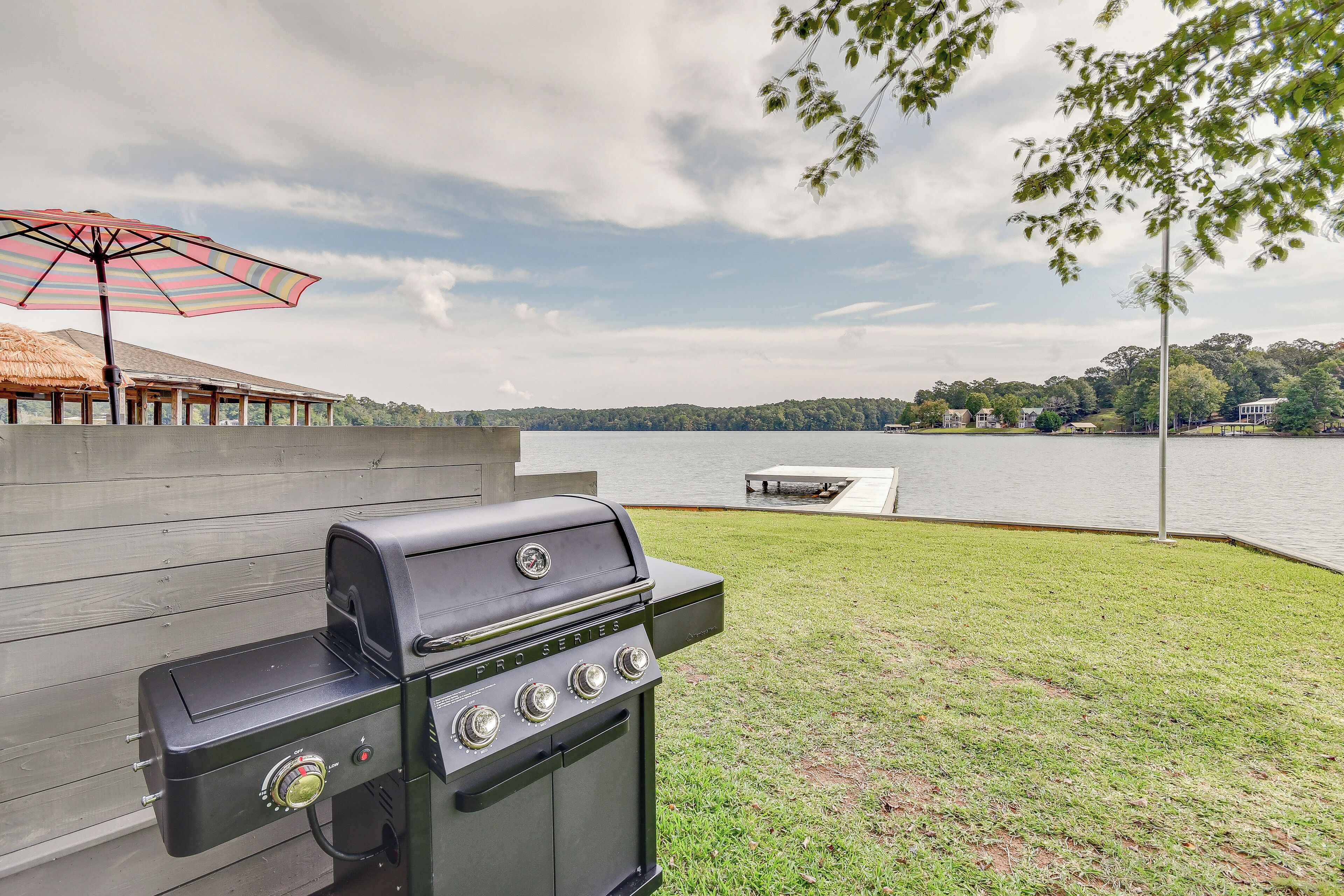 Een achtertuin met een barbecue, een constructie met rieten dak en uitzicht op een meer.