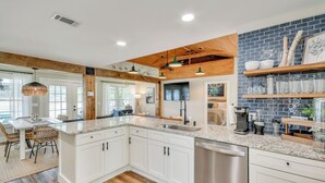 Eine moderne Küche mit weißen Schränken, Granit Arbeitsplatten und einem Geschirrspüler. Es gibt einen Essbereich mit Tisch und Stühlen, sowie ein Wohnzimmer mit Sofa und Couchtisch.