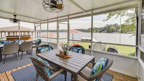 Eine überdachte Terrasse mit Tisch und Stühlen, große Fenster mit Blick auf einen See und Bäume.