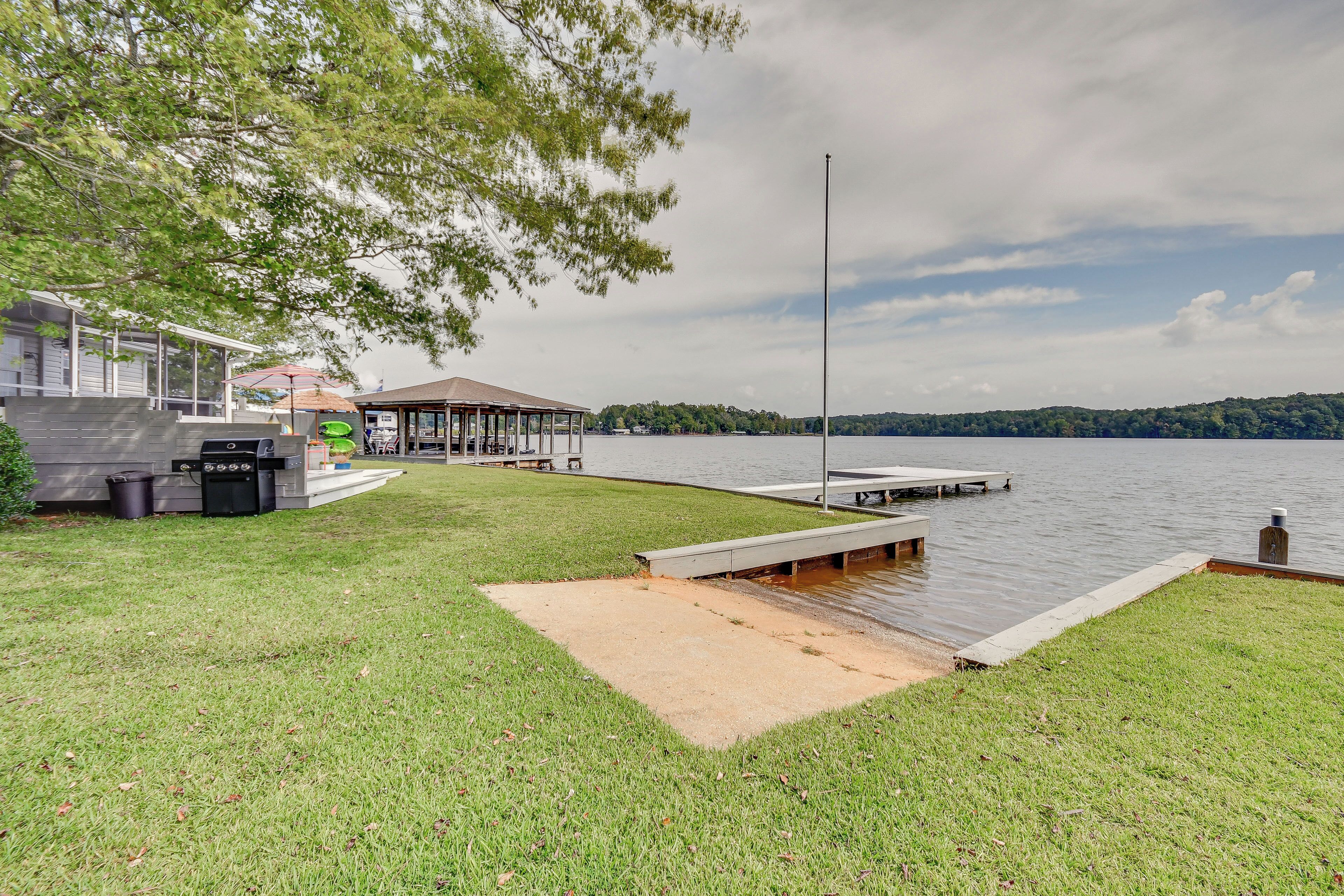 A lakeside property with a dock, a covered seating area, and a grassy lawn.