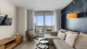 Un salon moderne avec un canapé, un fauteuil, un téléviseur et un balcon offrant une vue agréable.