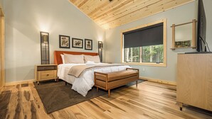 A bedroom with a wooden ceiling, a bed with white bedding, a nightstand, a dresser, and a window with a view of trees. - Black Diamond Lodge by Taylor Made Deep Creek (McHenry)