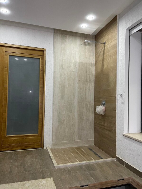 Un baño con puerta de madera, ducha con mampara de vidrio y pared blanca con textura.