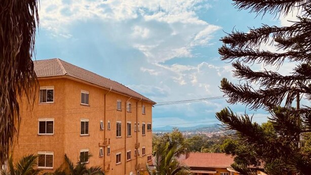 A multi-story building with a swimming pool, surrounded by palm trees and a clear sky. - Admiral hotel (Kampala)