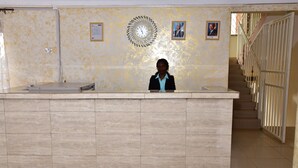 A reception desk with a clock, framed pictures, and a staircase in the background. - Admiral hotel (Kampala)