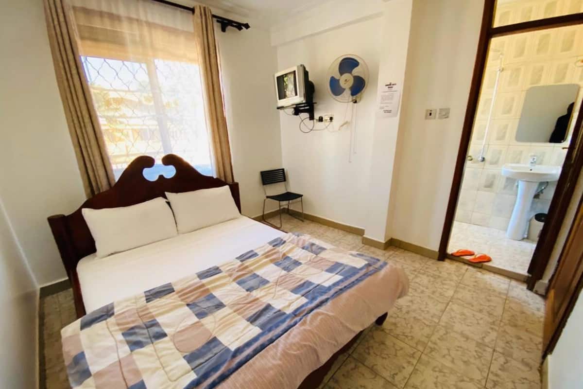 A hotel room with a bed, a TV, a fan, and a bathroom visible through an open door.