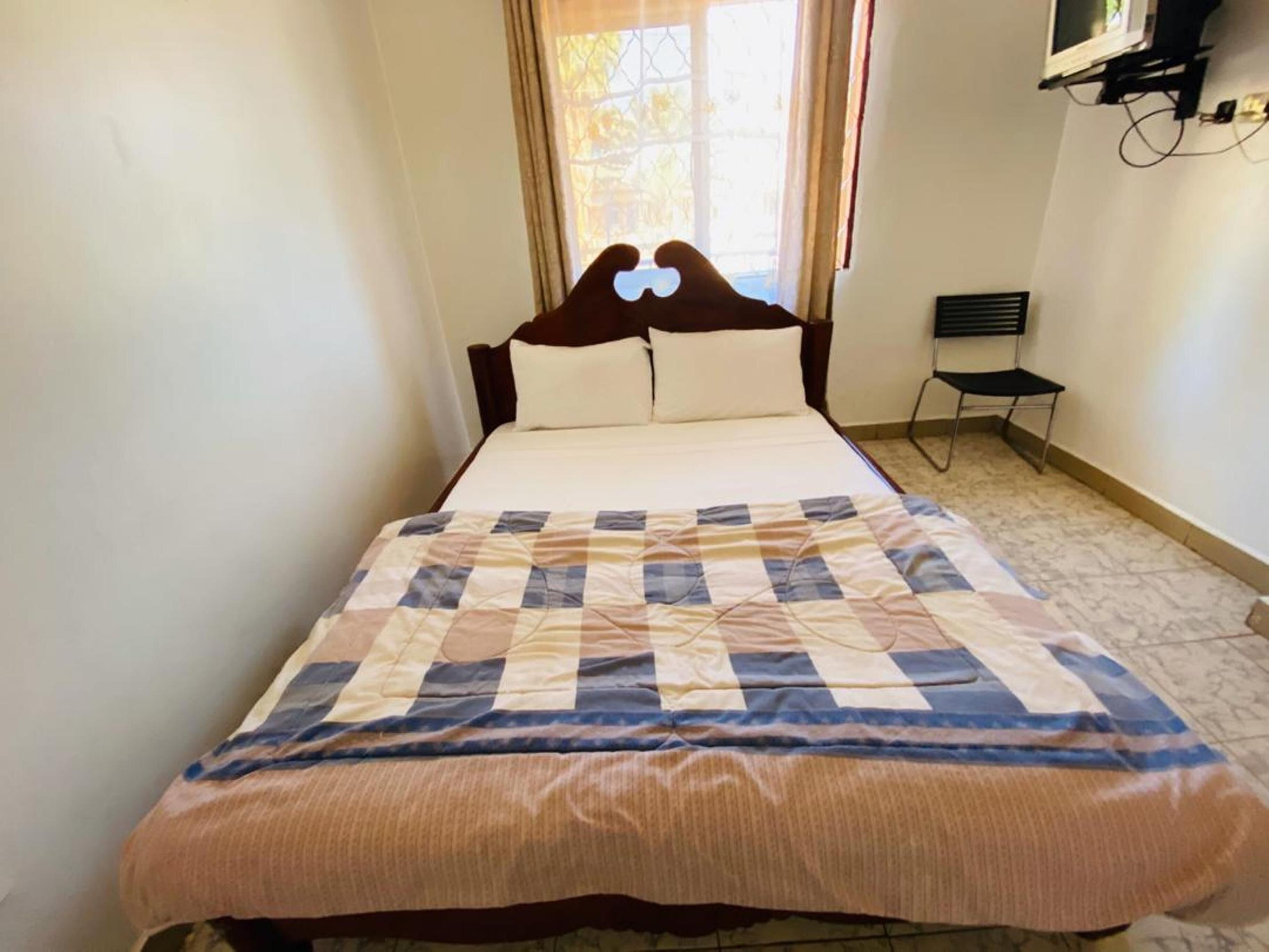 A neatly made bed with a checkered bedspread, a small bedside table, and a window with curtains.
