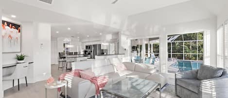 A modern living room with a glass coffee table, white sofas, and a pool area visible through large windows.